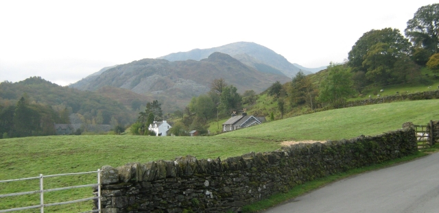 a typical lakeland view of steep hills and mountains in the background and a quiant house in a field